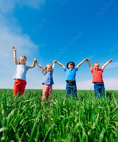 Happy Children on a green field with their hands up.