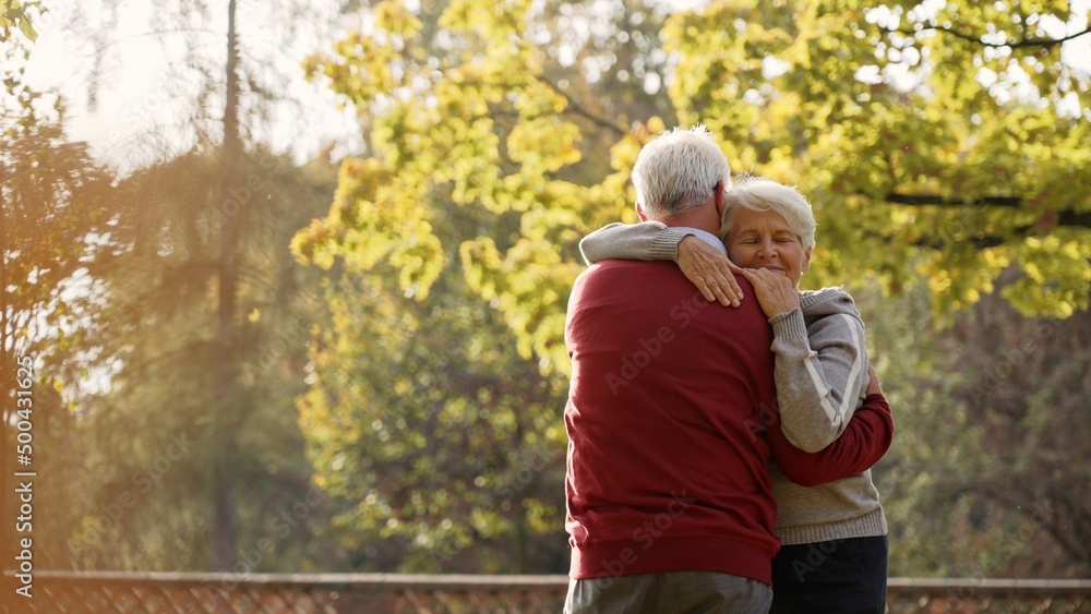 Naklejka premium European elderly gray-haired retired couple embracing each other after spontaneous dance in the park. Autumn vibes. High quality photo