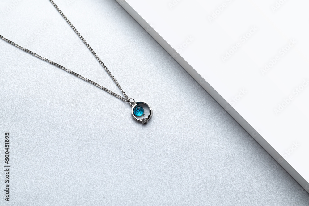 Fototapeta premium Silver chain necklace with blue diamond pendant on white background