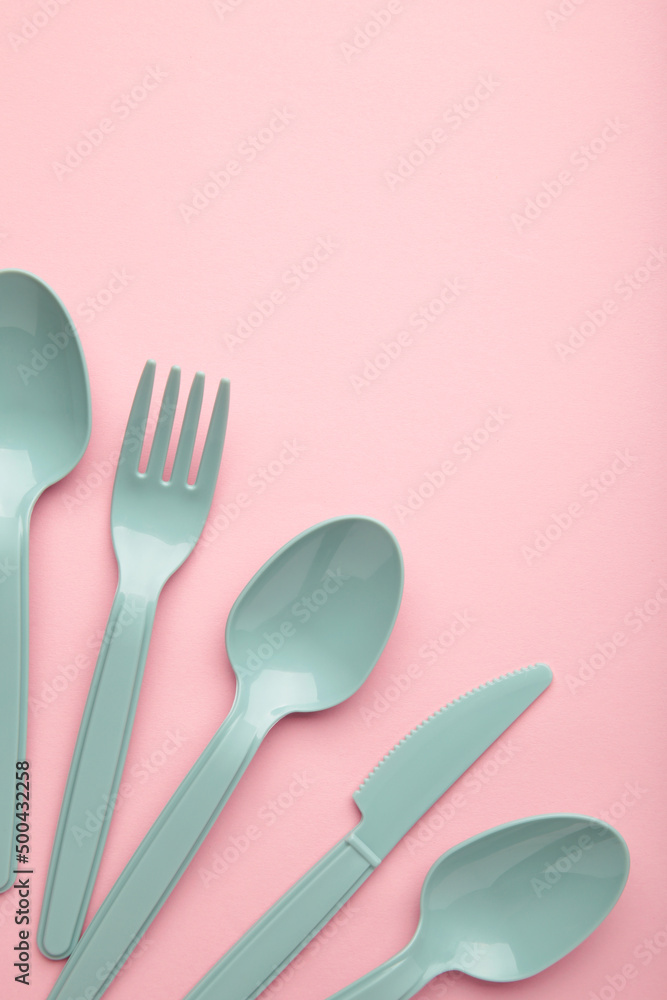 Many blue plasic forks, spoons and knives on pink background with copy space, top view. Many blue plasic forks, spoons and knives on pink background with copy space, top view.