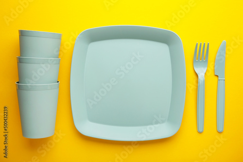 Bright plastic disposable tableware on yellow background.