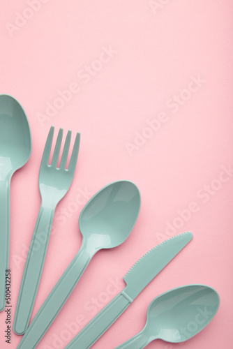 Many blue plasic forks, spoons and knives on pink background with copy space, top view.