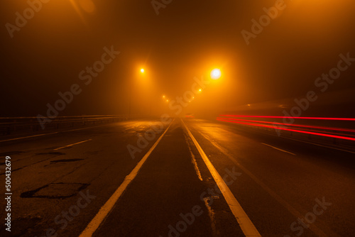 Night paved foggy road under the light of lanterns.