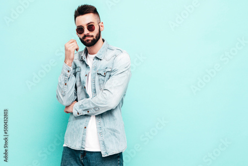 Portrait of handsome confident stylish hipster lambersexual model.Man dressed in jacket and jeans. Fashion male posing near wall in studio in sunglasses. Isolated