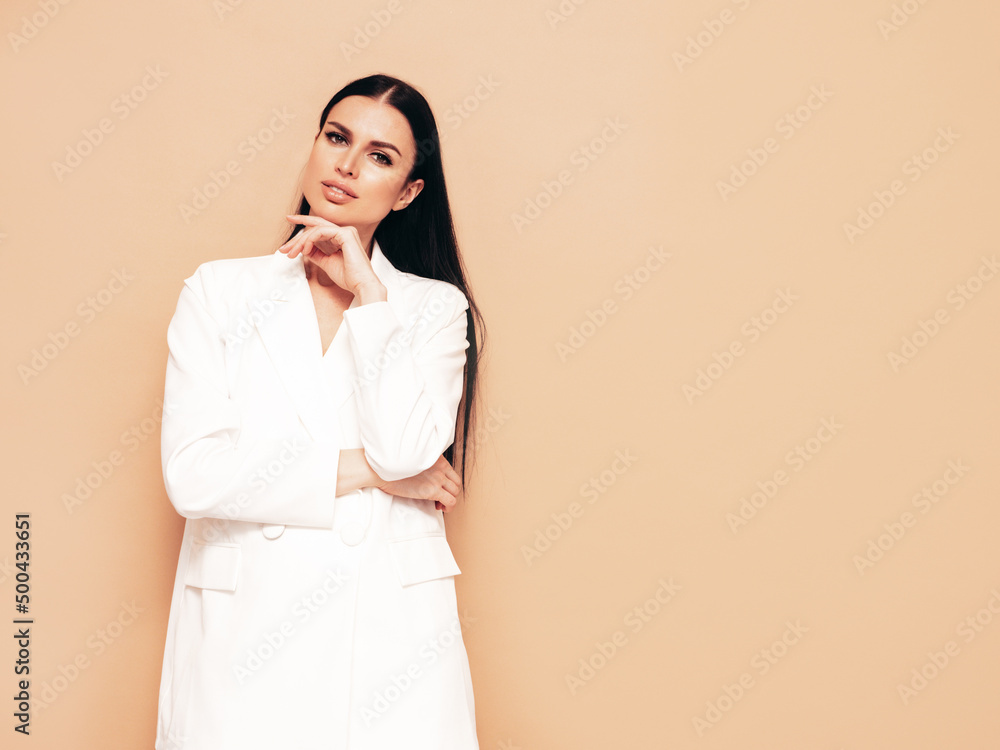 High fashion portrait of young beautiful brunette woman wearing nice trendy white suit. Sexy fashion model posing in studio. Fashionable female isolated on beige High fashion portrait of young beautiful brunette woman wearing nice trendy white suit. Sexy fashion model posing in studio. Fashionable female isolated on beige