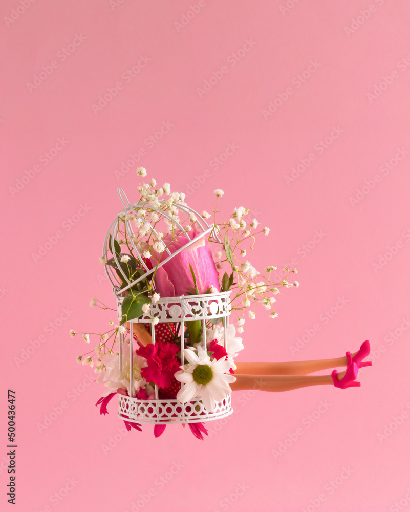 Woman legs and various spring flowers in the cage. Floral composition against pastel pink background. Minimal creative concept for perfect life but very little freedom.