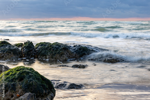 Beautiful blue waves splashing on the big rocks with a beautiful dramatic sunset in the backround.At the coast of Cap Blanc-Nez, France. High quality photo