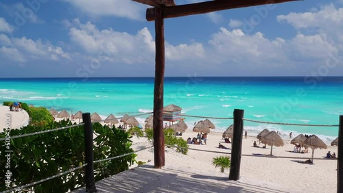 Picturesque view of turquoise sea and sandy Playa Delfines with parasols and tourists from wooden terrace on cloudy day in Cancun, Mexico