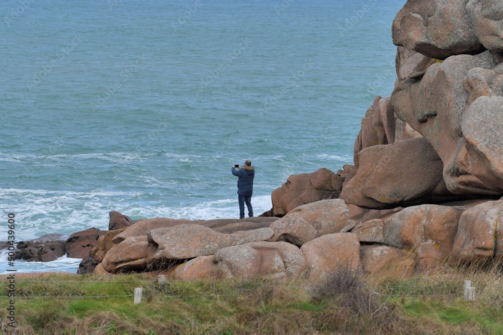 A man is taking a picture at the pink granite coast in Brittany France