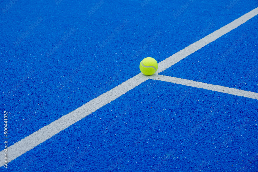 a ball on the lines of a blue paddle tennis court, racket sports concept