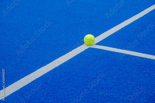 a ball on the lines of a blue paddle tennis court, racket sports concept © Vic