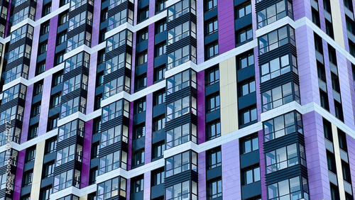 The facade of the building in purple,geometric patterns from windows and balconies, the colored wall of a modern multi-storey residential building, the abstract texture of the facade of the house