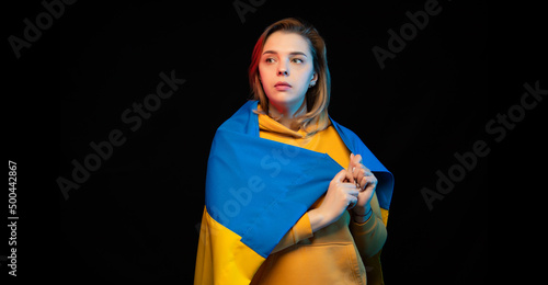 Beautiful Ukrainian girl with the national state flag of Ukraine on black background. Copy space. Russian Ukrainian War. Help and Pray for Ukraine. Stop war.