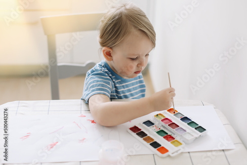 Child painting and drawing with watercolor paint at white table. Development of creative potential in children. 