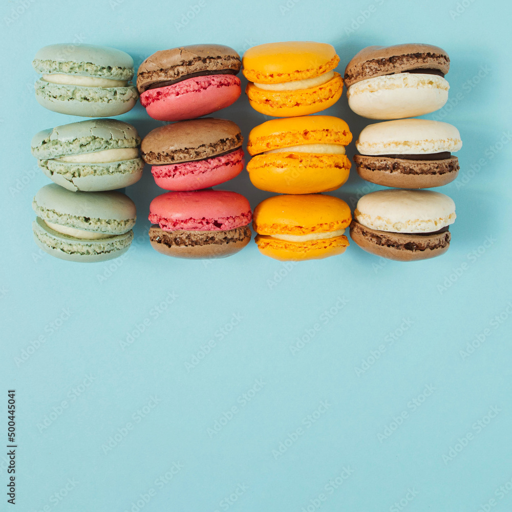 Fototapeta premium Pastel blue table top with colorful makarons pattern. The concept of minimal sweet food. Cookie concept