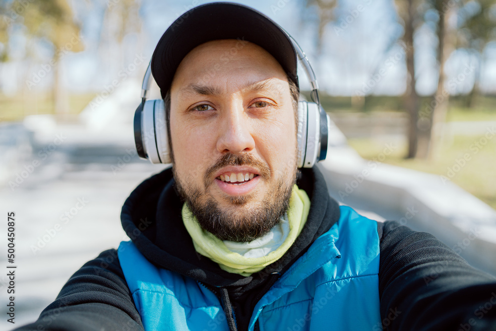 Athlete has video conversation on phone with friend, coach, man dressed in sports clothes and wireless headphones takes photo, records video of running practice. Athlete has video conversation on phone with friend, coach, man dressed in sports clothes and wireless headphones takes photo, records video of running practice.