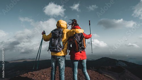Back view of a couple of hikers with backpack and poles watching the panorama from the peak of mount Etna in Sicily, Italy - the major European active volcano