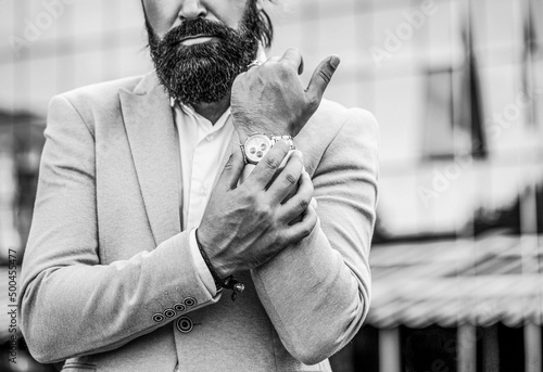 Watch in a man. Businessman points to his watch on the background of the town. Man holds his watch. Portrait successful businessman in a business suit, using the watch on a city background
