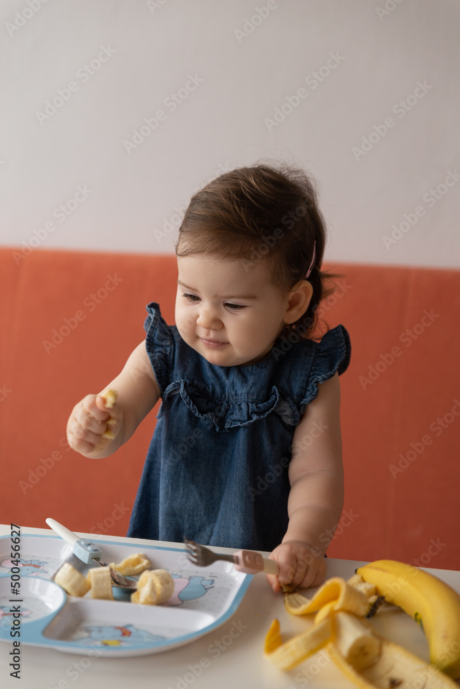 Pretty cute baby girl eating first food banana at home. Pretty cute baby girl eating first food banana at home.