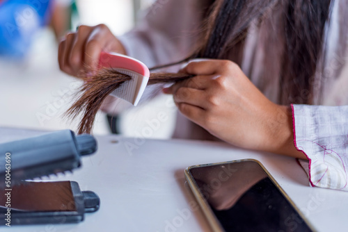 Damaged Hair, frustrated asian young woman, girl hand in holding brush splitting ends messy while combing hair, unbrushed dry long hair. Health care beauty concept. photo