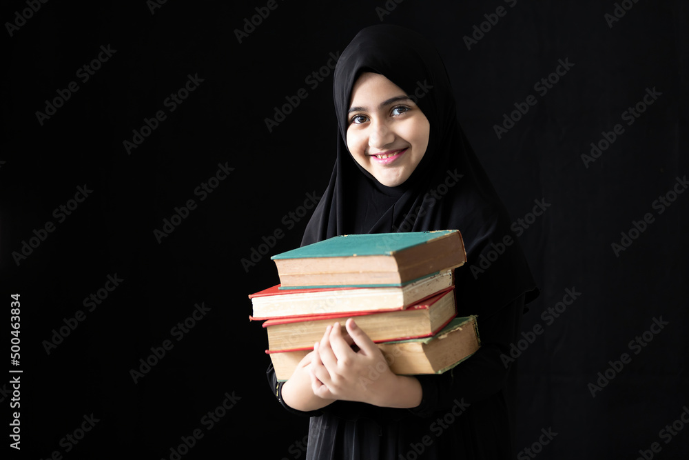 muslim girl holding a pile of books on black background muslim girl holding a pile of books on black background