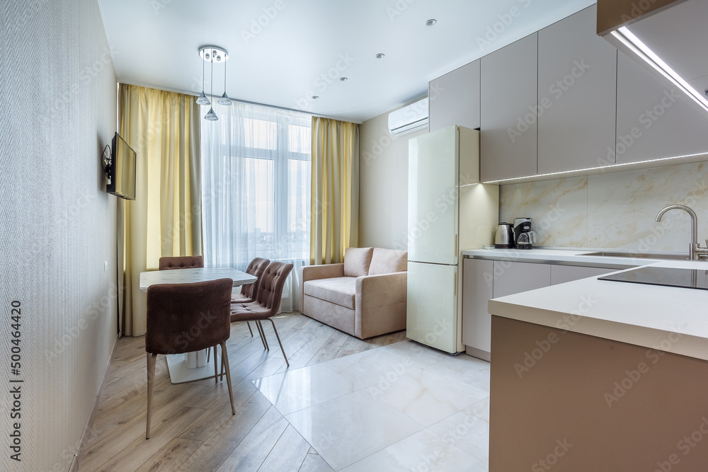 Modern beige and gray stylish kitchen with a table, soft chairs, a sofa and a beige refrigerator. Floor tiles and laminate. Built in household appliance Modern beige and gray stylish kitchen with a table, soft chairs, a sofa and a beige refrigerator. Floor tiles and laminate. Built in household appliance