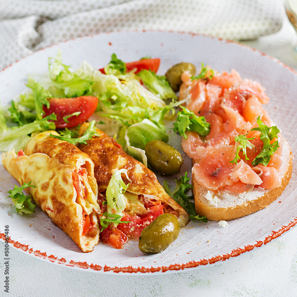 Breakfast. Omelette roll with tomatoes and sandwich with salmon on white plate. Lunch. Breakfast. Omelette roll with tomatoes and sandwich with salmon on white plate. Lunch.