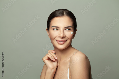 Beautiful smiling young woman applying face cream and looking away