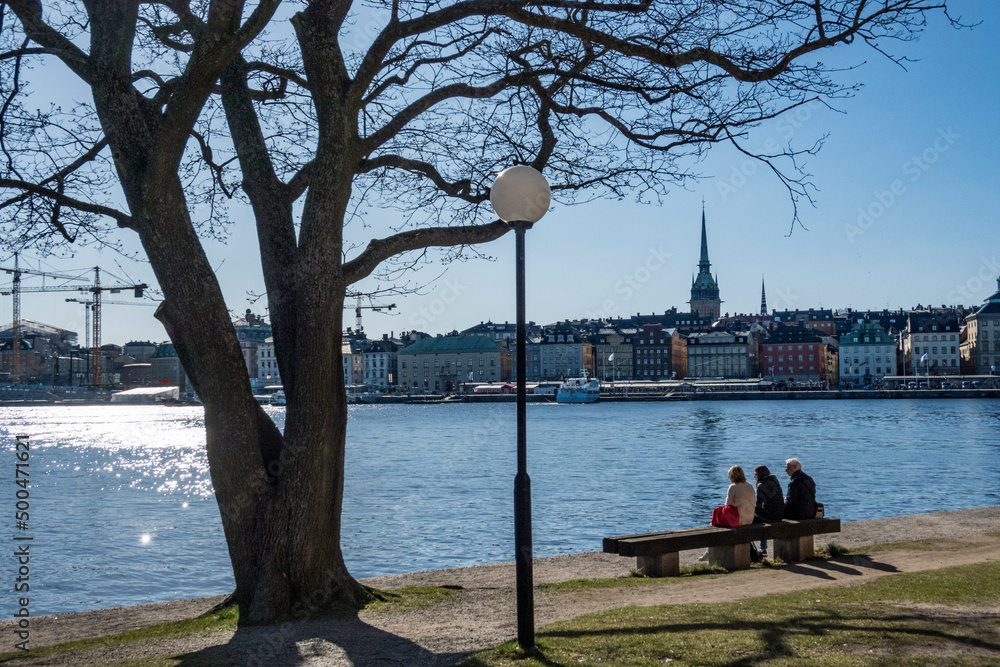 Stockholm, Sweden People sitting on a bench admiring view of Old Town Or Gamla Stan from the historic Skeppsholmen island.