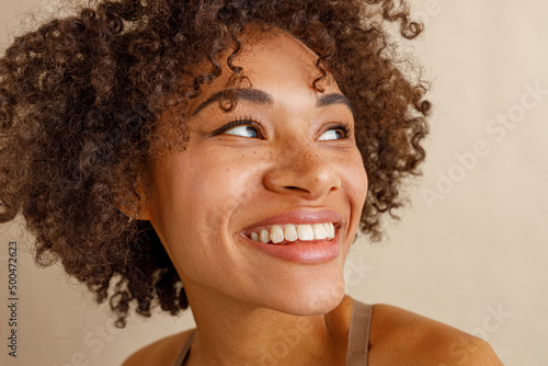 Multiethnic woman toothy smiling on beige background of studio