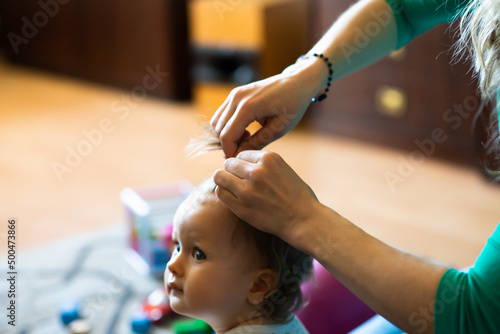 mother corrects baby girl hair at natural home blurred background