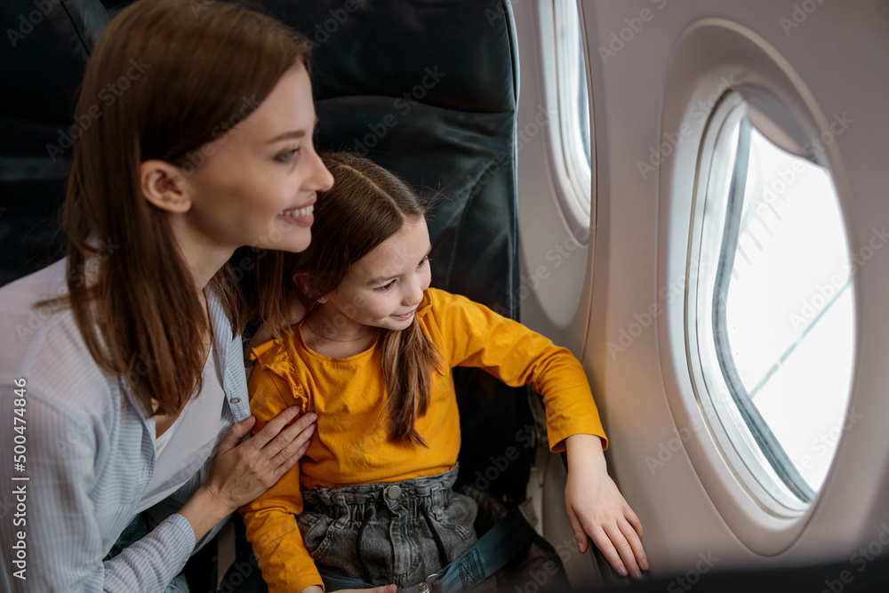 Fototapeta premium Cheerful mother and daughter looking out airplane window