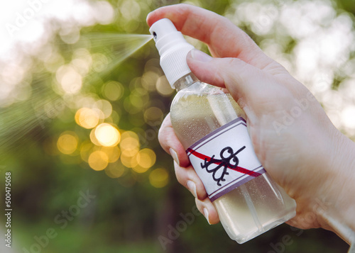 Close up view of woman hand holding and using DIY homemade essential oil based mosquito repellent outdoors in forest in the evening.