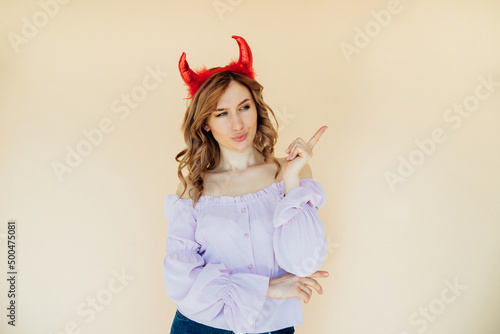 Portrait of a girl with wavy hair, in a devil costume for Halloween near a beige wall.