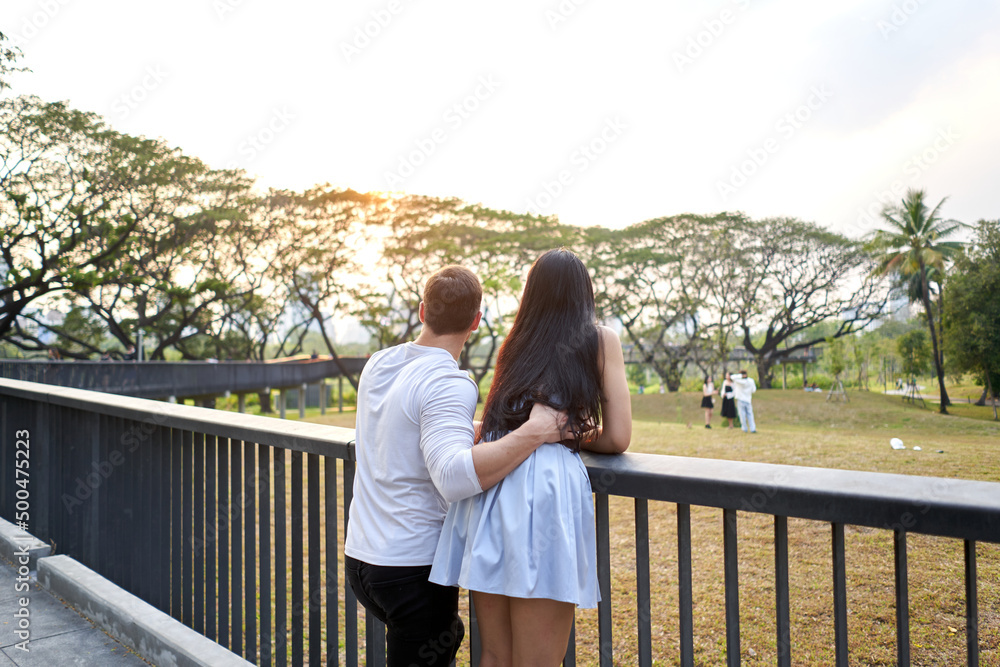 Multicultural couple looking the landscape of a park during sunset Multicultural couple looking the landscape of a park during sunset