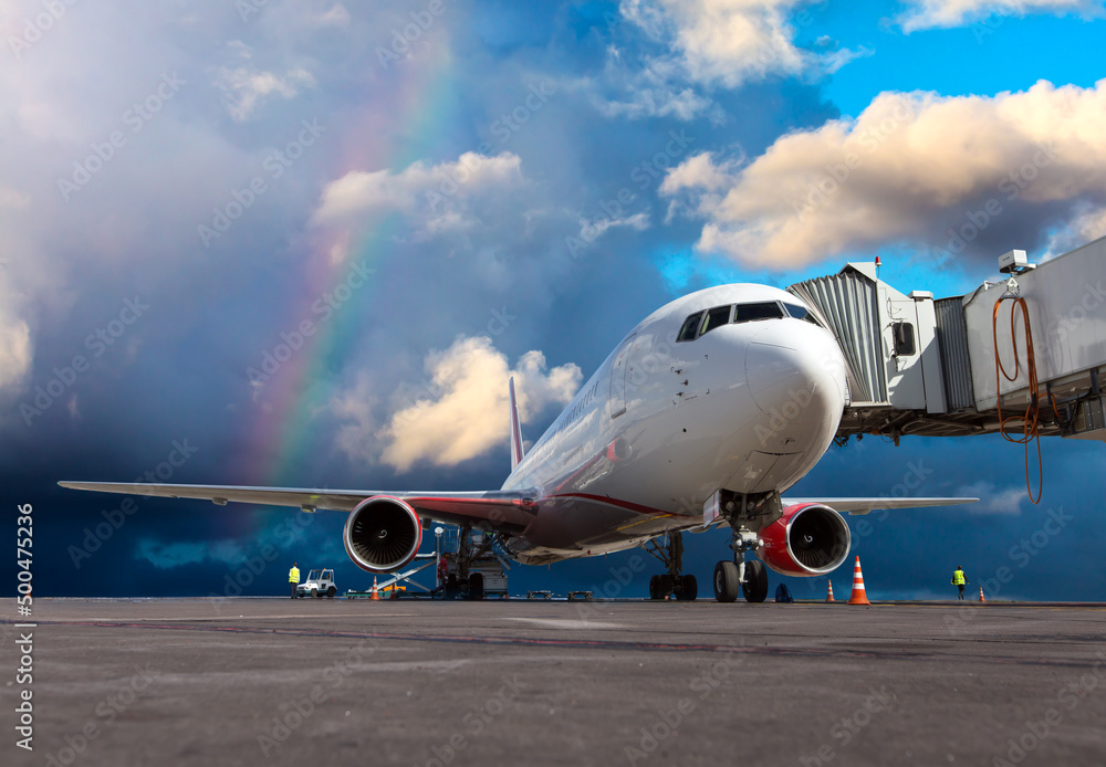 Passenger airplane at the airport runway against a bright blue sky and a rainbow. The plane is preparing for the flight. Passenger airplane at the airport runway against a bright blue sky and a rainbow. The plane is preparing for the flight.