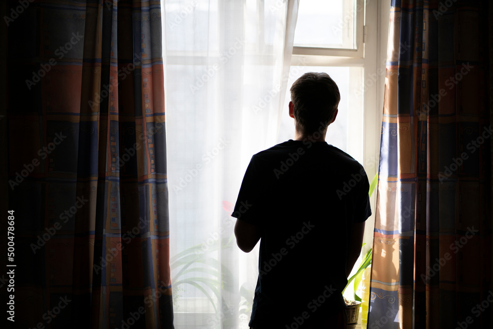 Fototapeta premium back view of man standing in front of the window in the morning at home, silhouette