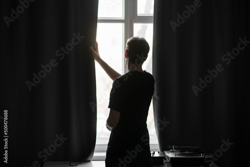 back view of man standing in front of the window in the morning at home, silhouette