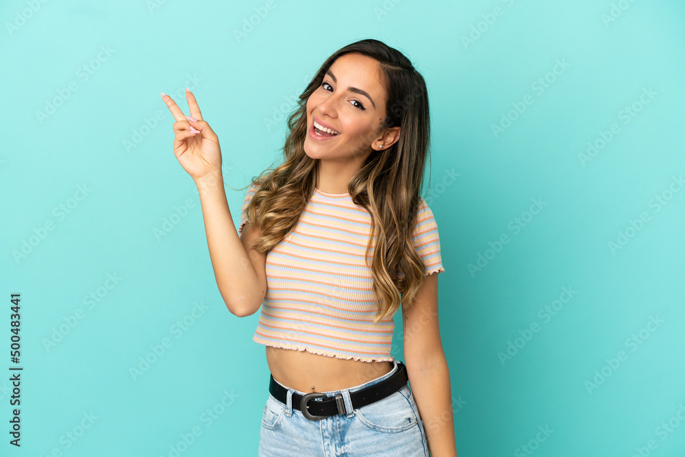 Young woman over isolated blue background smiling and showing victory sign Young woman over isolated blue background smiling and showing victory sign