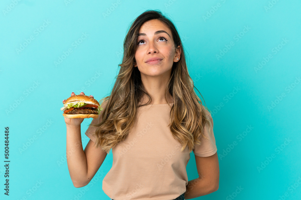 Young woman holding a burger over isolated background and looking up Young woman holding a burger over isolated background and looking up