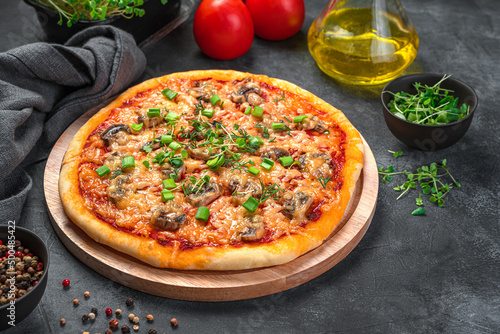 Homemade pizza with mushrooms, cheese, tomatoes and fresh herbs on a dark background.