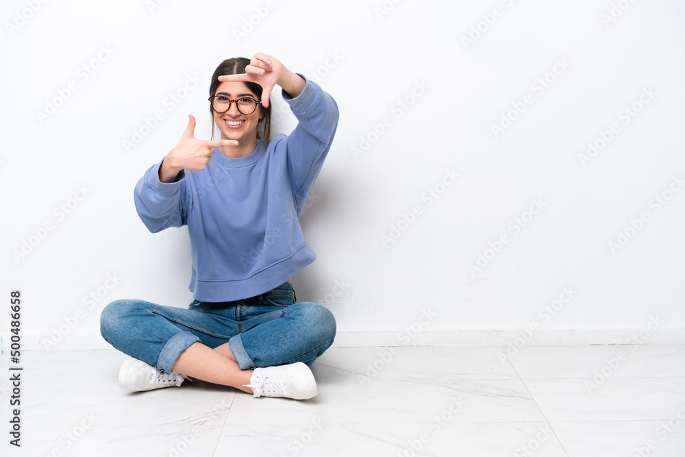 Young caucasian woman sitting on the floor isolated on white background focusing face. Framing symbol Young caucasian woman sitting on the floor isolated on white background focusing face. Framing symbol