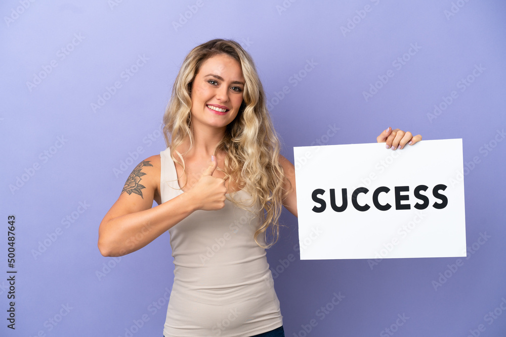 Young Brazilian woman isolated on purple background holding a placard with text SUCCESS with thumb up Young Brazilian woman isolated on purple background holding a placard with text SUCCESS with thumb up