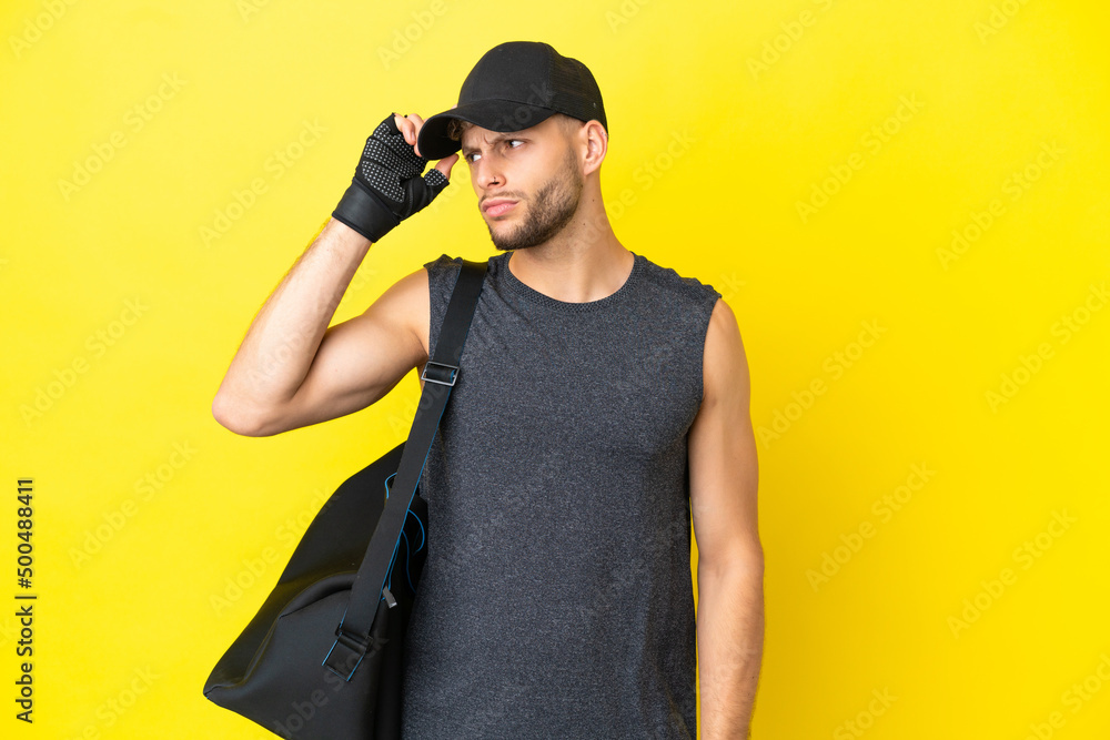 Young sport blonde man with sport bag isolated on yellow background having doubts and with confuse face expression Young sport blonde man with sport bag isolated on yellow background having doubts and with confuse face expression