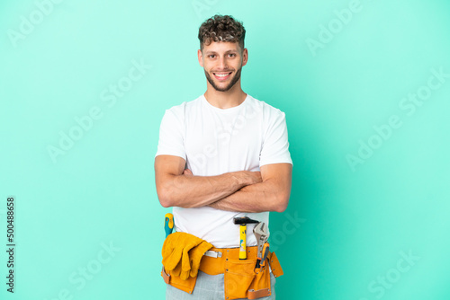 Young electrician blonde man isolated on green background keeping the arms crossed in frontal position