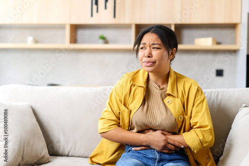 Fotografia Young African-American woman sitting on the couch and suffers from month menstru