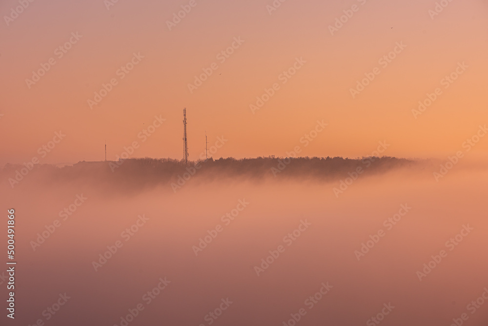 Communication masts on a hill surrounded by dense fog.