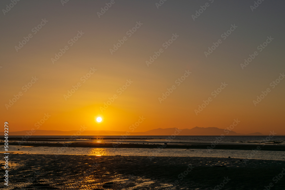 Sunset over the beach and mountain, horizon line yellow and orange shadiing reflection to water and sand. Focusing at surface shadow. Landscape nature scenery background.