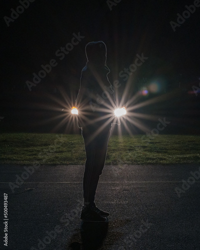 a young man stands in front of car headlights forming a star pattern on a dark night photo