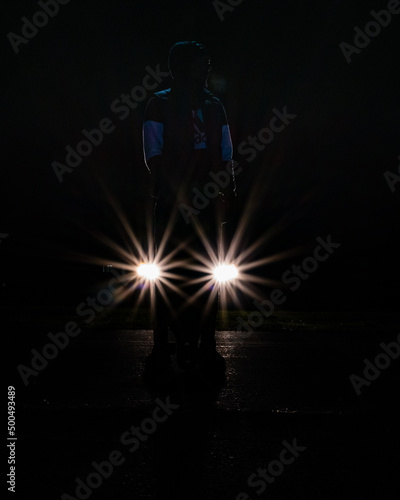 a young man stands in front of car headlights forming a star pattern on a dark night